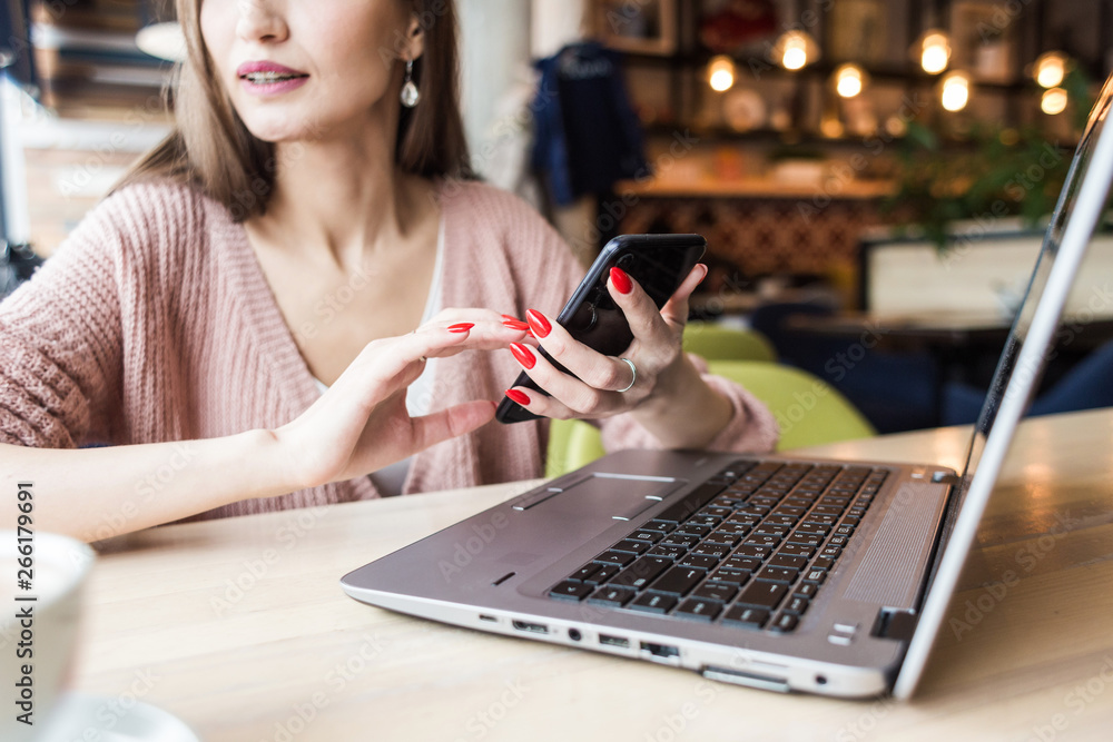Attractive young woman sits at a table in a cafe with a cup of coffee and a laptop and uses the phone Attractive young woman sits at a table in a cafe with a cup of coffee and a laptop and uses the phone