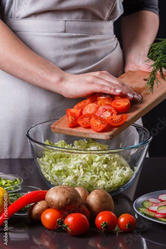 young woman in a gray apron adds cherry tomatoes to a salad