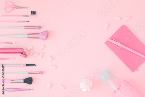 Feminine accessories with unicorn makeup brushes on pink background and water bottle notebook with pen. Flat lay with copy space, birthday beauty and cosmetics blogger concept