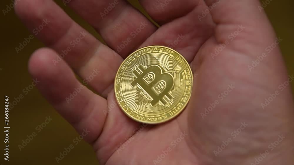 Gold bitcoin coin on the male palm which is squeezed into a fist. Bitcoin business concept. Close up of bit coin in hand. Investment in bitcoin cryptocurrency business. Global blockchain technology Gold bitcoin coin on the male palm which is squeezed into a fist. Bitcoin business concept. Close up of bit coin in hand. Investment in bitcoin cryptocurrency business. Global blockchain technology