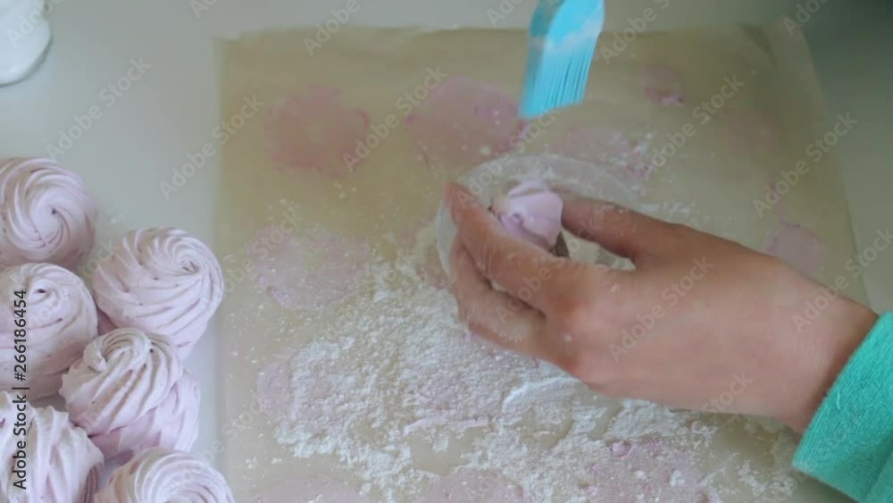 A woman treats marshmallows with powdered sugar using a pastry brush. View from above.. A woman treats marshmallows with powdered sugar using a pastry brush. View from above..