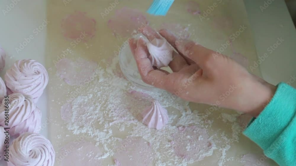 A woman treats marshmallows with powdered sugar using a pastry brush. View from above A woman treats marshmallows with powdered sugar using a pastry brush. View from above