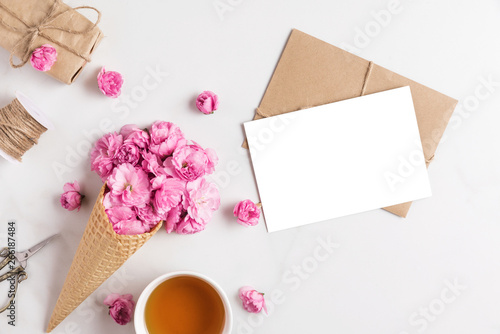blank greeting card and ice cream cone of pink blossom cherry flowers in waffle cone with cup of tea and gift box