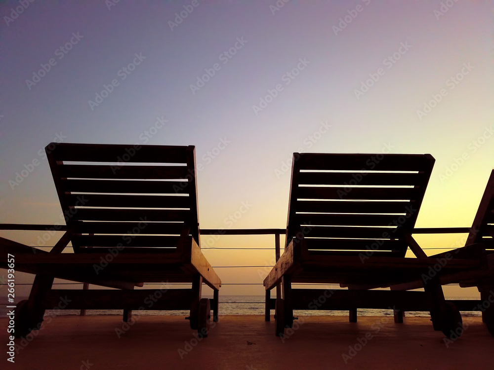 Tropical background with couple of deck chairs at sunset by sea. It is beautiful view of golden sun.