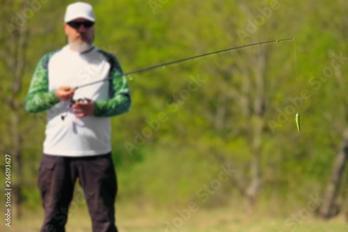 Selective focus photo of fisherman with spinning rod and focus at artificial lure