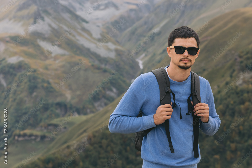 Fototapeta premium Young tourist man with a backpack against the background of the Caucasus Mountains, Georgia on a foggy day