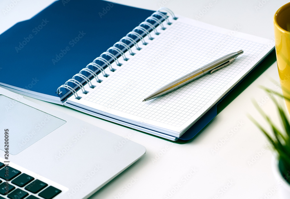 Closeup of white desktop with laptop, coffee cup, notepads, pen, calculator and other items. Closeup of white desktop with laptop, coffee cup, notepads, pen, calculator and other items.