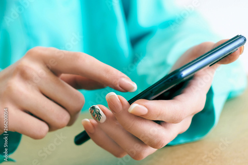 Young woman using smartphone for surfing and browsing Internet  searching for required information  sitting at desk with laptop.