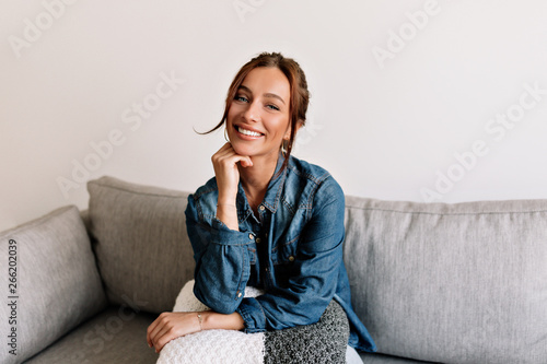 Obraz na płótnie Happy laughing girl with tanned skin and white teeth sitting at sofa at cosy apartment and posing at camera w salonie