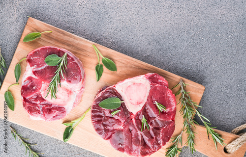 Sliced meat on a wooden board with herbs and spices. Raw meat on the bone close-up. Gray background. photo