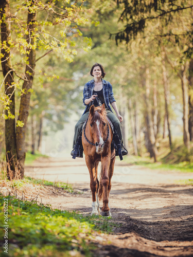 happy young woman riding horse with cordeo in the morning in spring forest