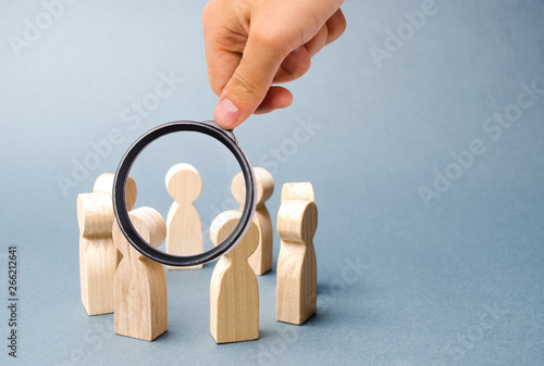 Magnifying glass is looking at people stand in a circle on a gray background. Wooden figures of people. A circle of people. discussion, cooperation, cooperation. teamwork, team spirit. Selective focus photo