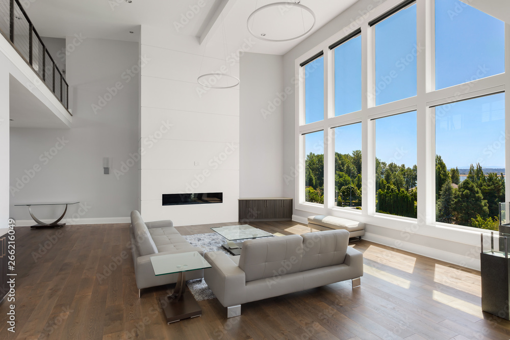 Beautiful modern living room in new luxury home with floor to ceiling fireplace surround and wall of windows with view Beautiful modern living room in new luxury home with floor to ceiling fireplace surround and wall of windows with view
