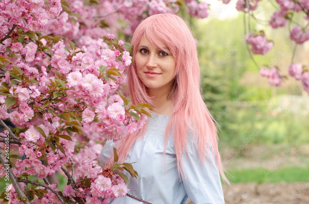 Girl with pink hair smiling and standing near sakura flowers Girl with pink hair smiling and standing near sakura flowers