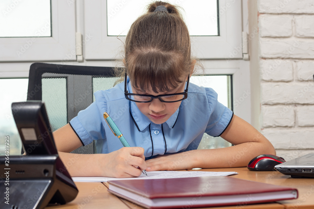 Naklejka premium An eight-year-old girl writes on a desk in an office setting
