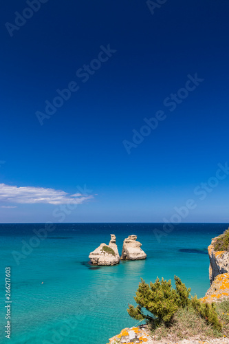 The bay of Torre dell'Orso, with its high cliffs, in Salento, Puglia, Italy. Turquoise sea and blue sky, sunny day in summer. The stacks called the Two Sisters. A person swims in the clear water