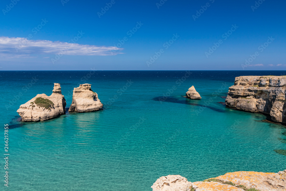 The bay of Torre dell'Orso, with its high cliffs, in Salento, Puglia, Italy. Turquoise sea and blue sky, sunny day in summer. The stacks called the Two Sisters, immersed in the sea.