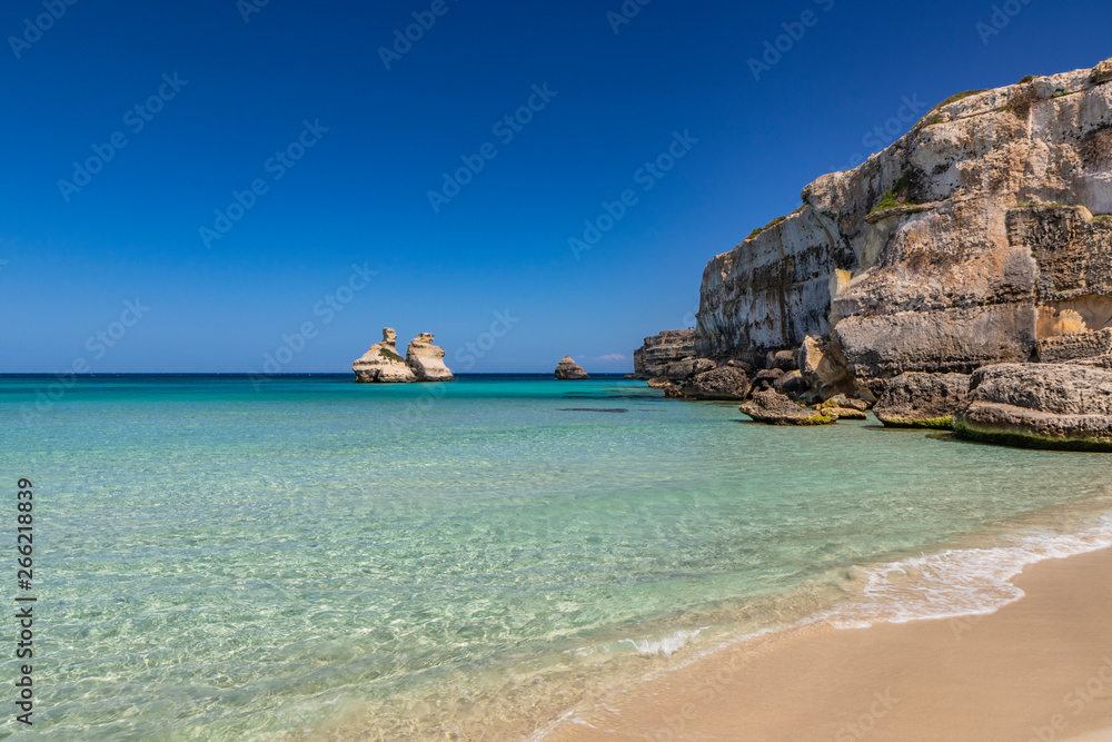 The bay of Torre dell'Orso, with its high cliffs, in Salento, Puglia, Italy. Turquoise sea and blue sky, sunny day in summer. A beach of fine white and pink sand. The stacks called the Two Sisters.