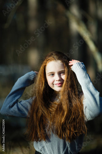 Portrait of cute twelve year old girl with fiery red hair posing in the pine park for a photoshoot.