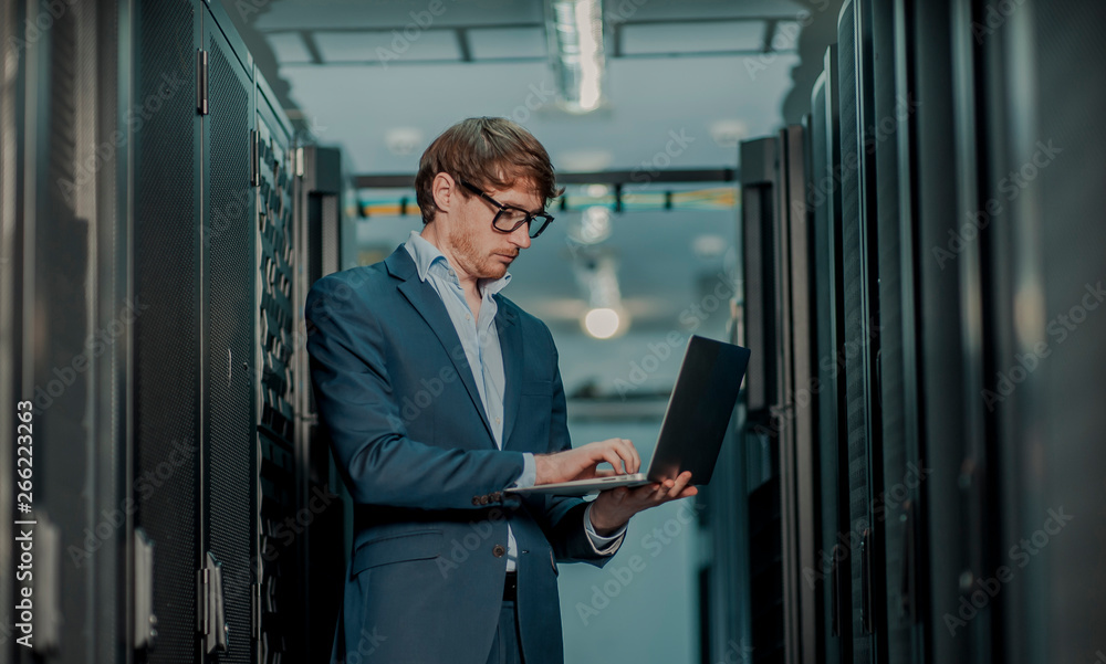 Young it engeneer business man with thin modern aluminium laptop in network server room Young it engeneer business man with thin modern aluminium laptop in network server room