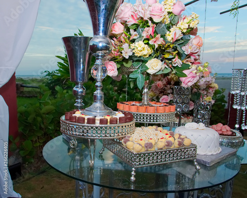  Decorated table for wedding with floral arrangement, sweets and cake. Beach in the background