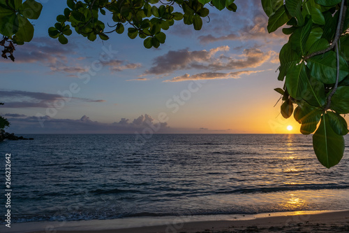 The sun kisses the horizon as it sets for the evening, leaving behind a glow of blue, pink and orange skies. Amazing sunset on Negril Jamaica beach. Idyllic romantic tropical Caribbean island setting.