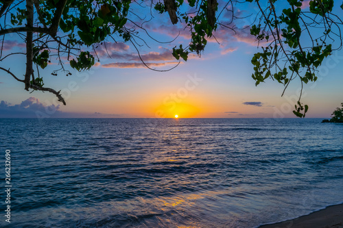 The sun kisses the horizon as it sets for the evening, leaving behind a glow of blue, pink and orange skies. Amazing sunset on Negril Jamaica beach. Idyllic romantic tropical Caribbean island setting. © Enrico
