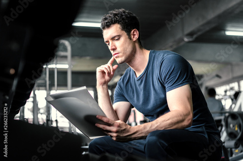 Fotografia, Obraz Muscular handsome trainer looking at fitness plan on clipboard for working out i