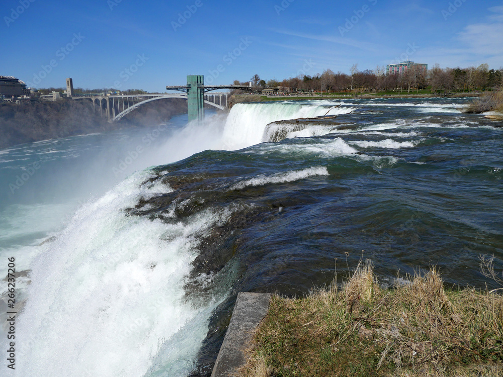 Niagara Falls, close up view of the edge of the waterfall with Rainbow Bridge and observation tower in the background Niagara Falls, close up view of the edge of the waterfall with Rainbow Bridge and observation tower in the background