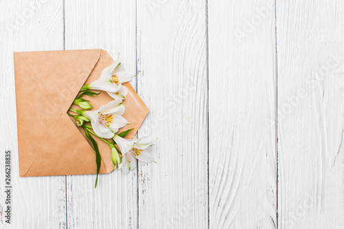 Flat lay with White lilies in craft envelope on old white wooden background