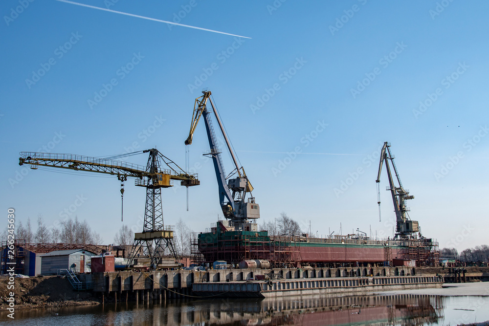 Dry cargo barge with cranes on it against the blue sky and a pair of jets