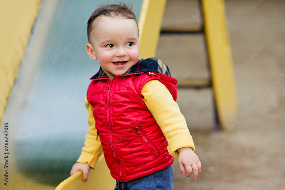 One-year-old boy plays on a playground next to a slide. He is smiling. One-year-old boy plays on a playground next to a slide. He is smiling.