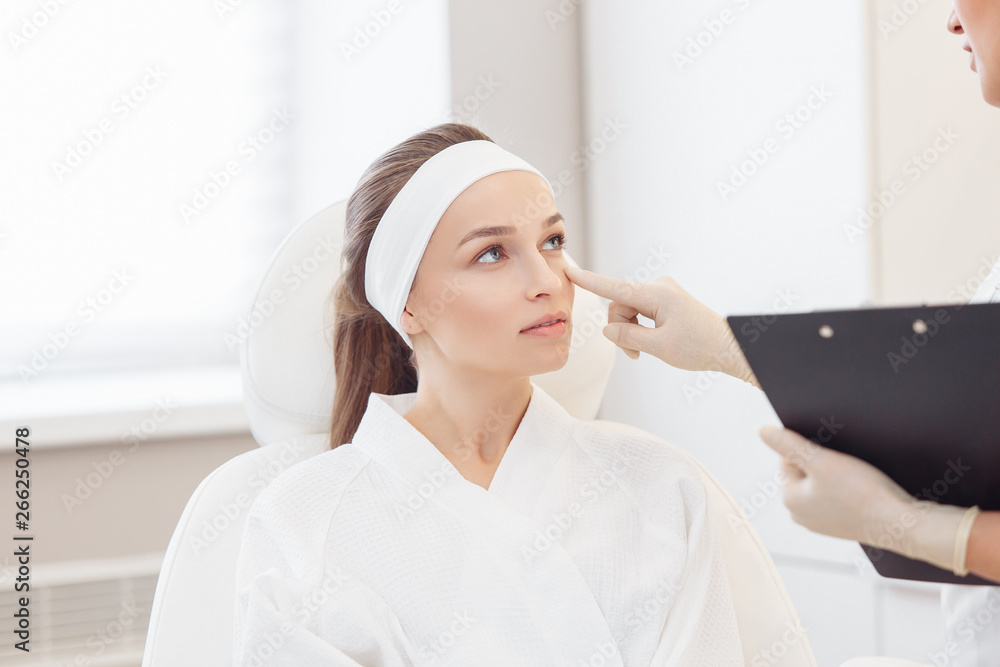 Young pretty woman came to a beauty salon and consults with a beautician on anti-aging treatments. Self care concept Young pretty woman came to a beauty salon and consults with a beautician on anti-aging treatments. Self care concept