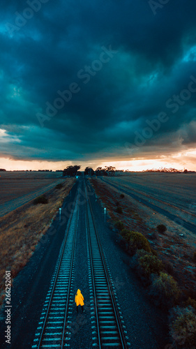 Person in Yellow Jacket on Old Train Tracks With Epic Sky