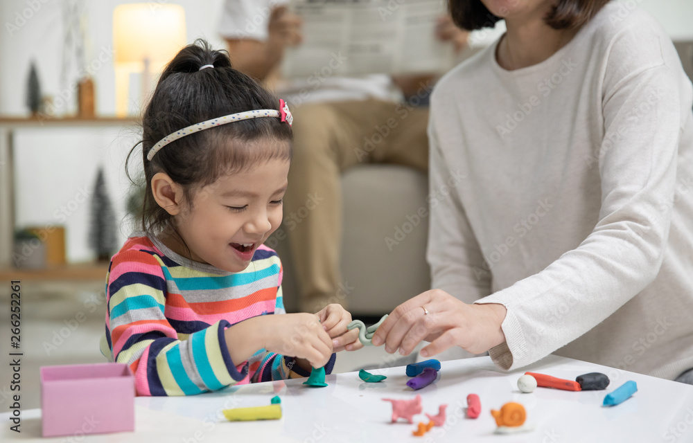 Mom with her daughter playing with a colorful toys modeling clay on the floor, at background daddy is sitting in a sofa in the living room, Happy asian family at home Mom with her daughter playing with a colorful toys modeling clay on the floor, at background daddy is sitting in a sofa in the living room, Happy asian family at home