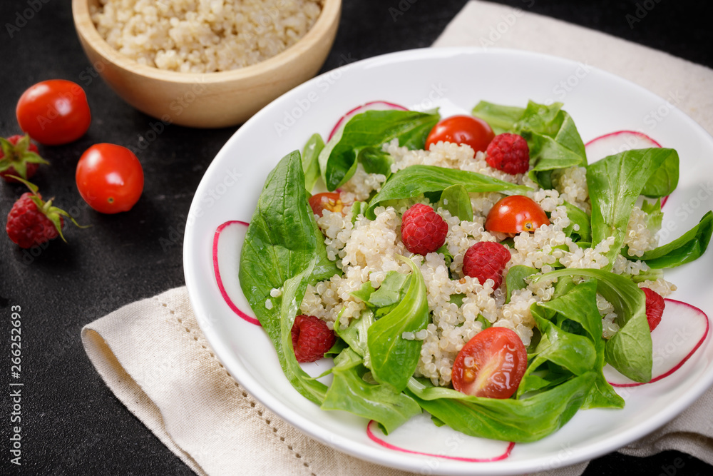 Quinoa salad with vegetables, raspberry and tomatoes on the black table. Super food for healthy and concept of balanced diet Quinoa salad with vegetables, raspberry and tomatoes on the black table. Super food for healthy and concept of balanced diet