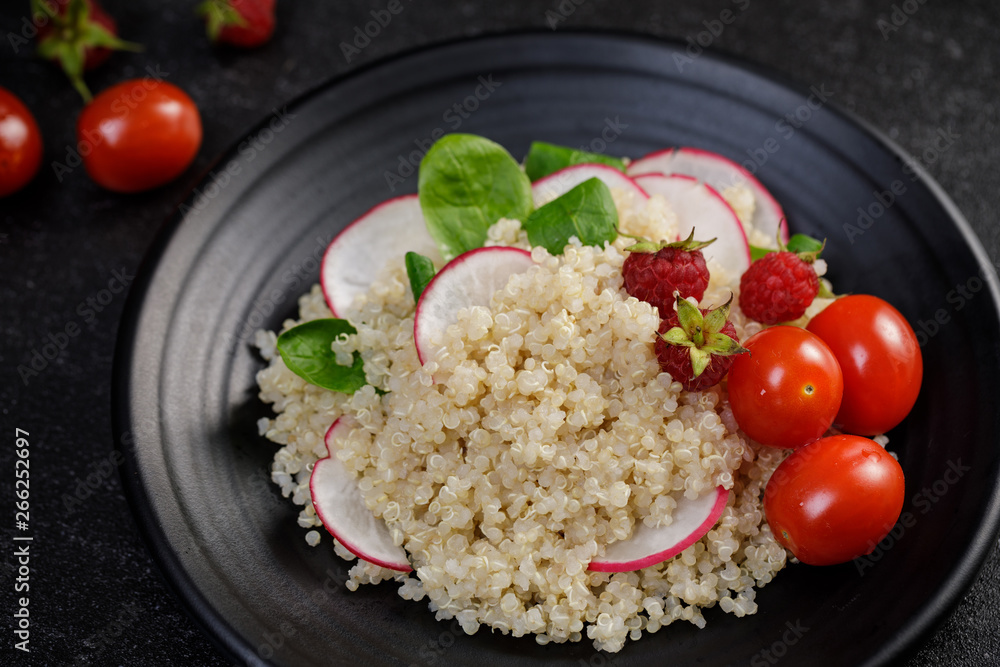 Quinoa salad with vegetables, raspberry and tomatoes on the black table. Super food for healthy and concept of balanced diet Quinoa salad with vegetables, raspberry and tomatoes on the black table. Super food for healthy and concept of balanced diet
