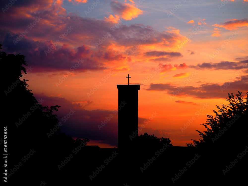 Silhouette of church in front of sunset and orange sky.