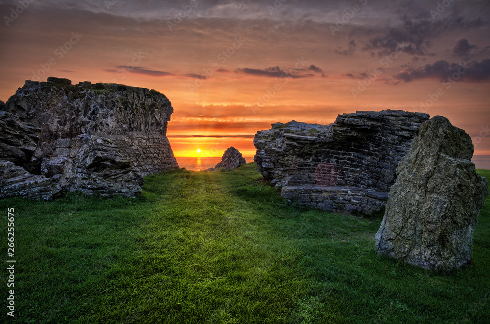 A romantic and beautiful view through the ruins of Aberystwyth Castle on the sunset on the horizon above the sea.