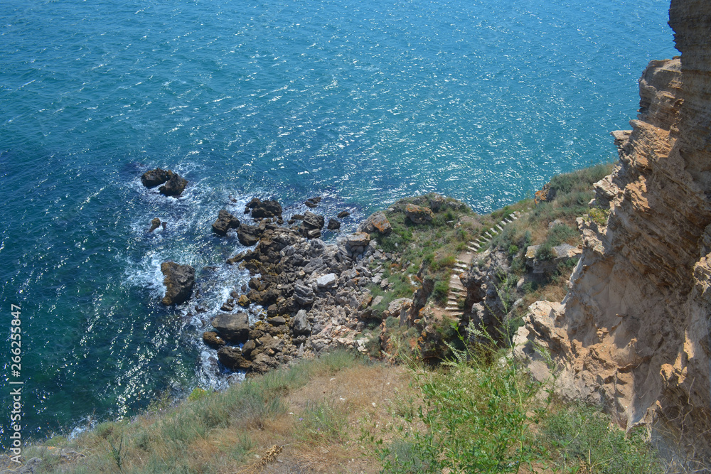 Beautiful top view of the rocky coast and stone stairs. Sunny day on the sea coast. Waves beat on the rocks below.