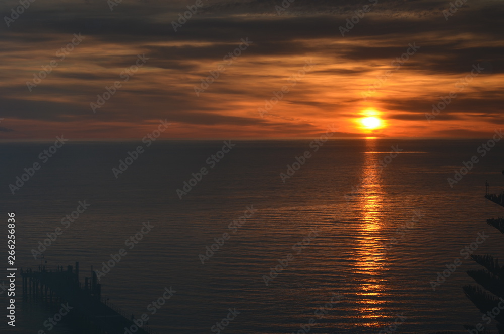 orange ocean sunset with gray clouds and jetty pier at Glenelg South Australia orange ocean sunset with gray clouds and jetty pier at Glenelg South Australia