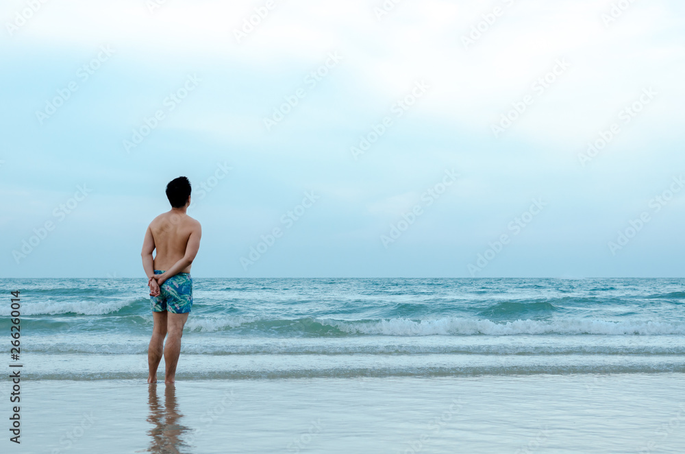 A lonely Asian man stand alone on beach facing to the sea in blue day.