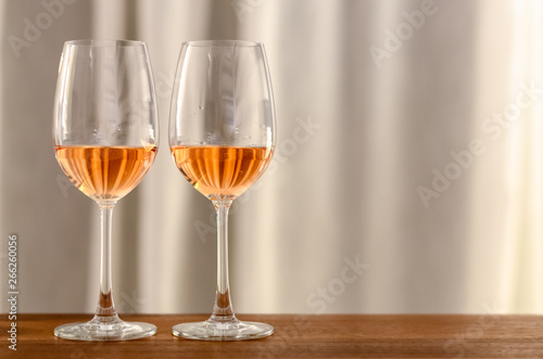 Two glasses of Rose wine on wooden table to celebrate for a couple with bright background of curtain in the house.