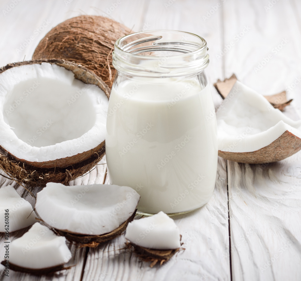 Milk or yogurt in mason jar on white wooden table with coconut aside Milk or yogurt in mason jar on white wooden table with coconut aside