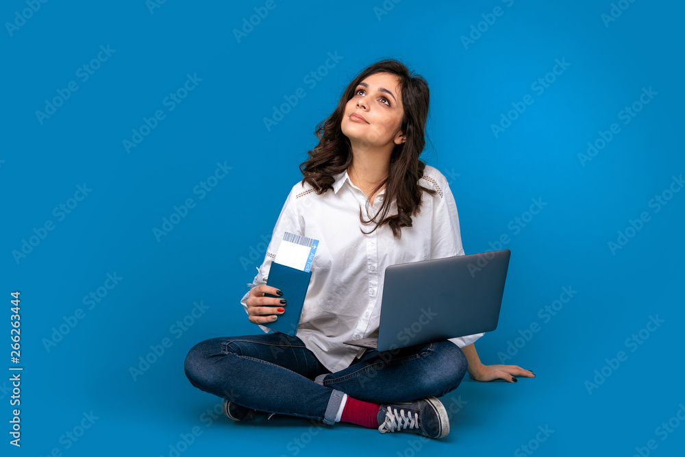 Young woman sitting on the floor with laptop and passport buying tichets online Young woman sitting on the floor with laptop and passport buying tichets online