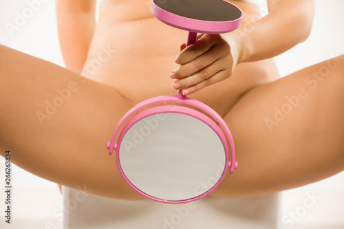 Woman looking at her vagina in the mirror on white background photo