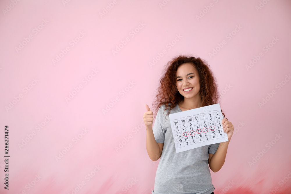African-American woman holding calendar with marked days of menstruation on color background African-American woman holding calendar with marked days of menstruation on color background