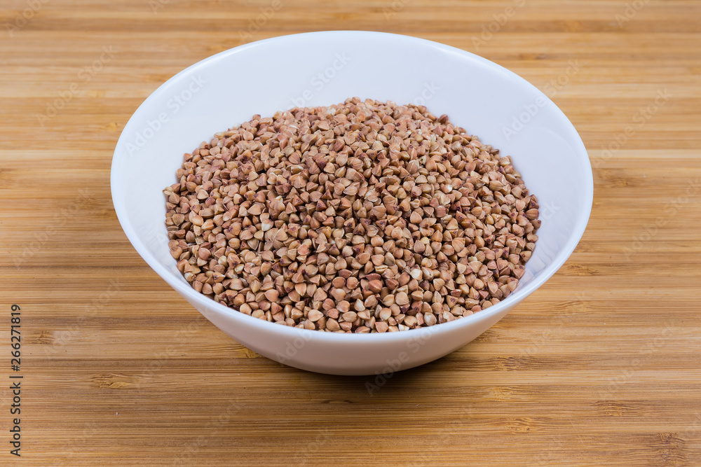 Bowl of uncooked pre-steamed buckwheat groats on wooden surface Bowl of uncooked pre-steamed buckwheat groats on wooden surface