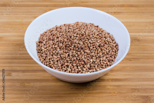Bowl of uncooked pre-steamed buckwheat groats on wooden surface