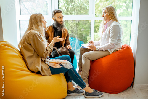 Young couple having misunderstandings during the psychological counseling with senior female psychologist in the office